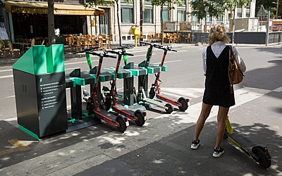 Une dame se tient devant une borne de recharge électrique pour trottinettes