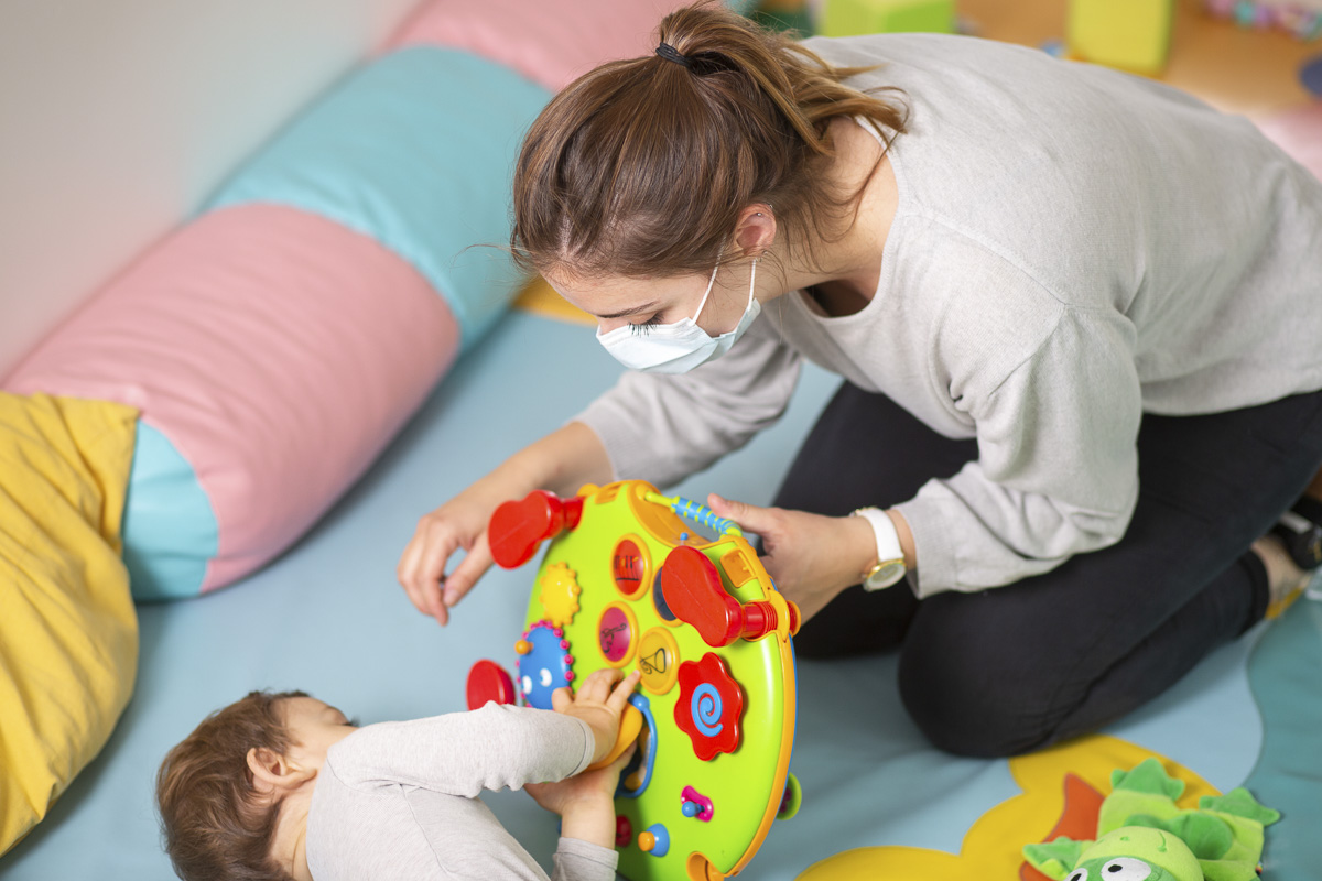 Auxiliaire de puériculture et de soin masquée avec un jeune enfant