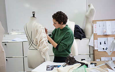 Une élève confectionne un vêtement sur mannequin.