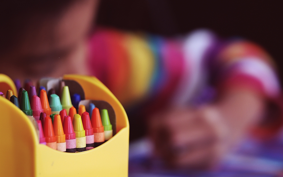 Crayons de couleurs en premier plan avec un enfant en train de dessiner, flou, en arrière-plan