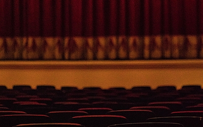 Fauteuils de théâtre vus de dos, avec en arrière-fond la scène et le rideau rouge fermé