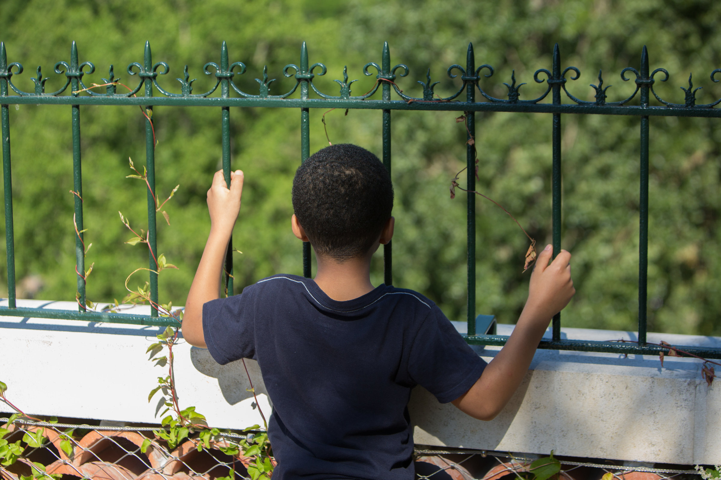 Un enfant se tient de dos devant une grille de jardin.