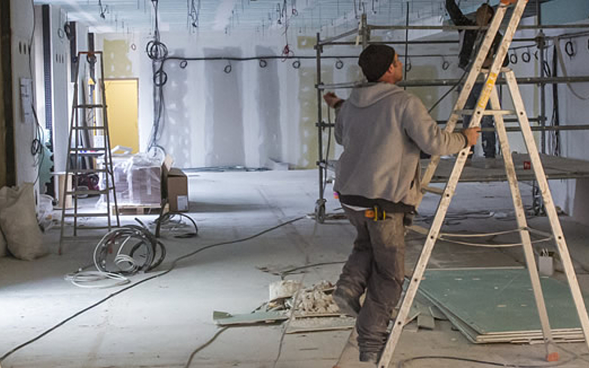 Deux ouvriers du bâtiment font des travaux, l'un est sur un échaffaudage, l'autre en train de monter sur une echelle