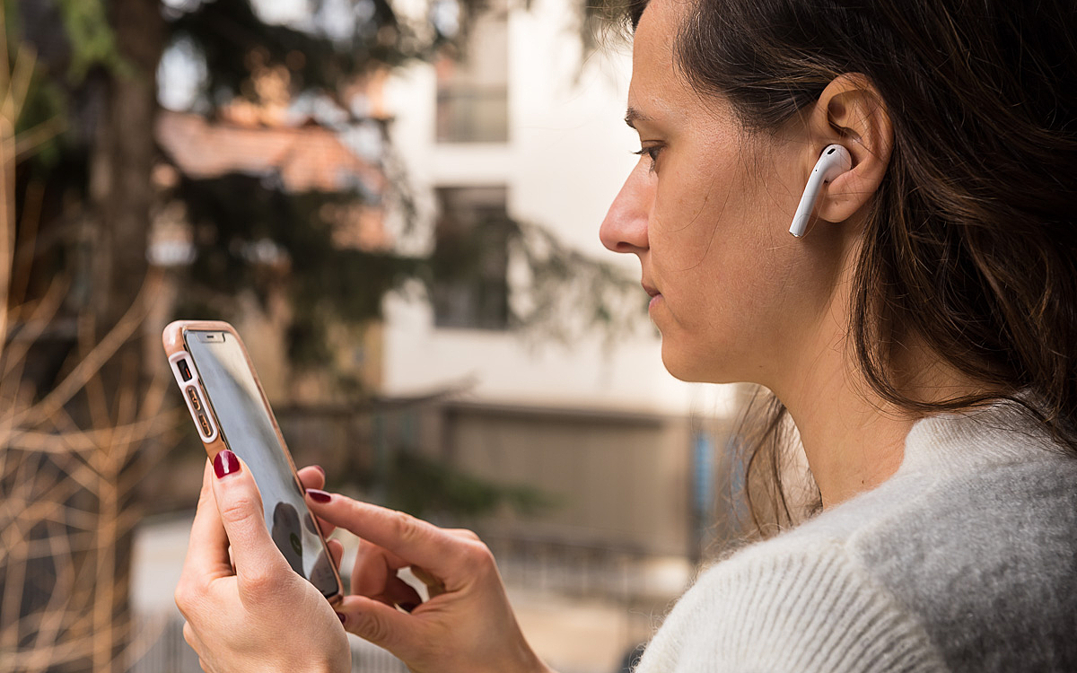 Une parisienne tient son téléphone portable dans la main et porte des oreillettes..