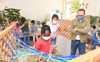 Journées des Arts Plastiques 2021 "Tissage" Une enfant observée en plein tissage de fil de laine par son professeur d'Arts Plastiques et Emmanuel Coblence (Conseiller de Paris délégué à l’éducation, aux nouveaux apprentissages et aux relations avec la Caisse des écoles). Lieu du reportage : Centre Paris Lecture, Corvisart, 13e