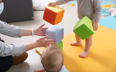 très jeunes enfants et un adulte jouant avec des gros cubes en mousse dans une crèche