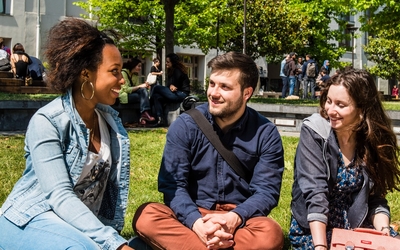 Trois jeunes étudiants discutent assis dans l'herbe. 