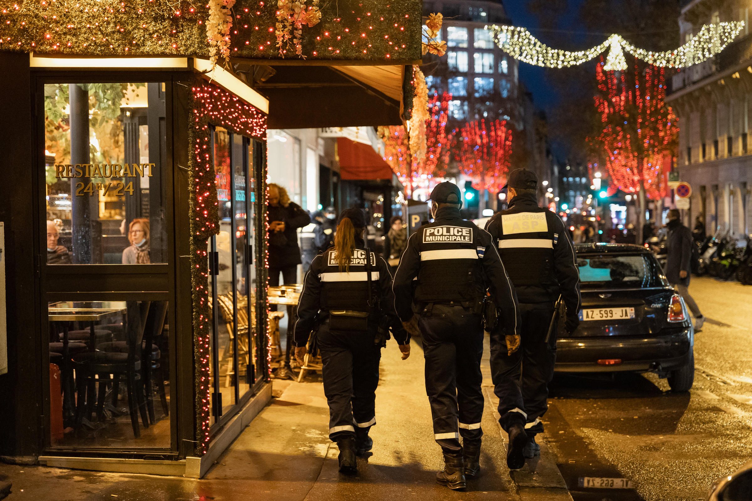Une patrouille de 3 policiers et policières municipales marchent dans Paris près d'un restaurant.