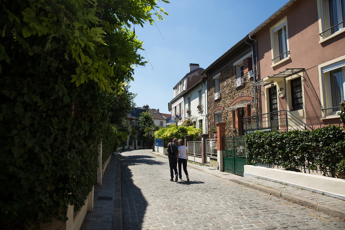 Un couple se promène dans une rue pavée et tranquille de "La Campagne à Paris" (20e)