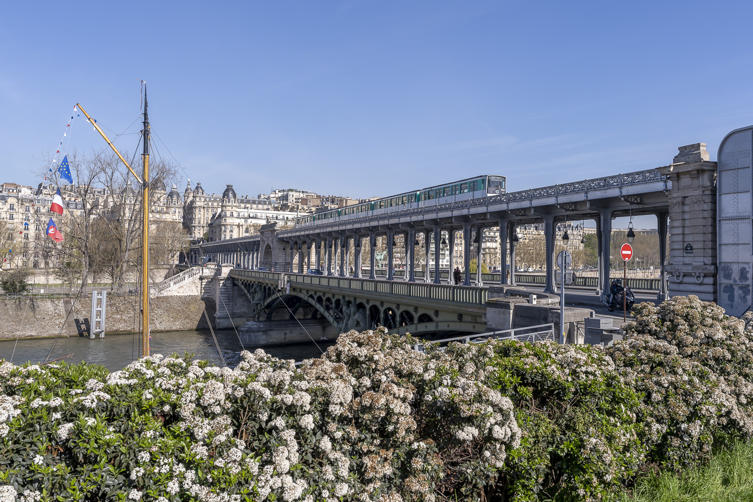 Des fleurs au premier plan et un pont au second plan sur lequel passe un métro aérien.