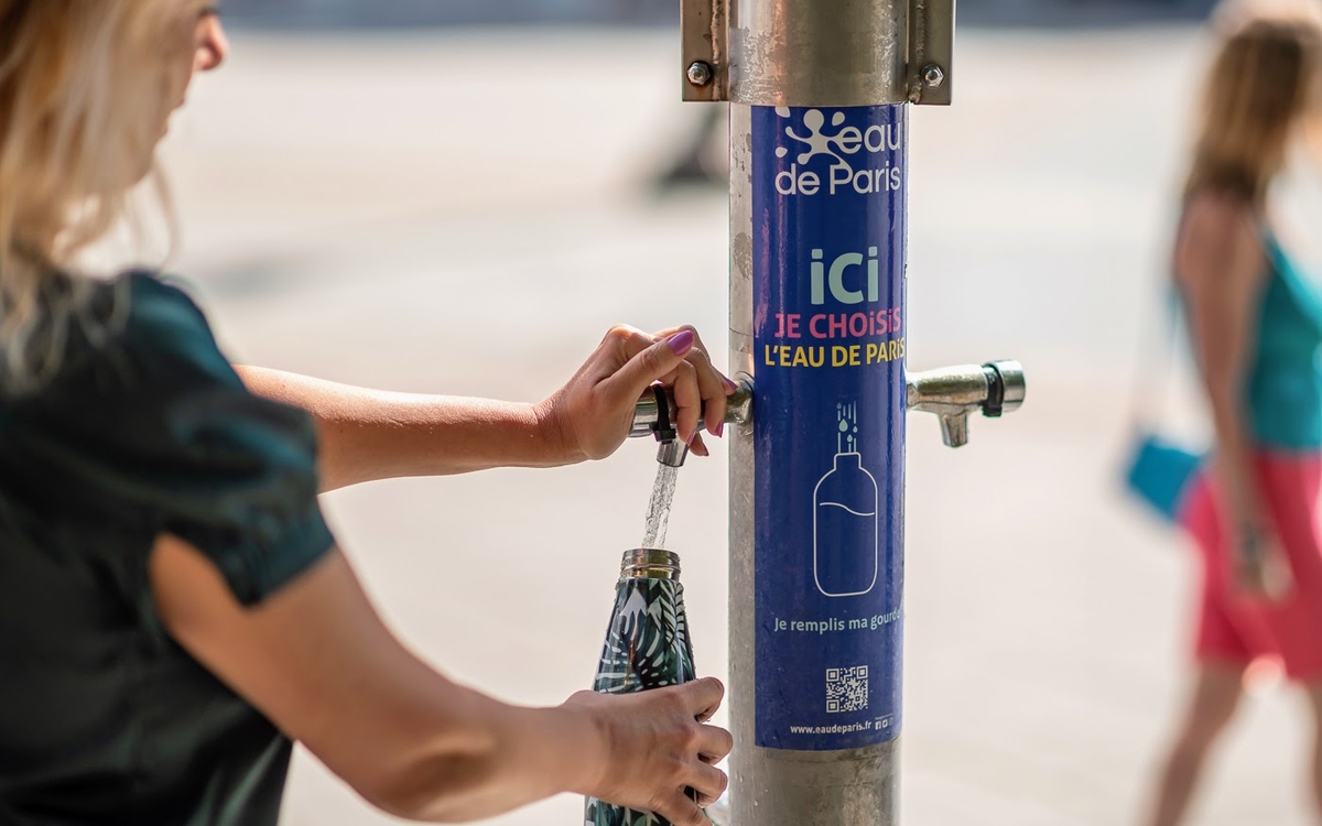 Jeune femme remplissant sa gourde d'eau potable, à une fontaine mise à disposition par la Ville de Paris.