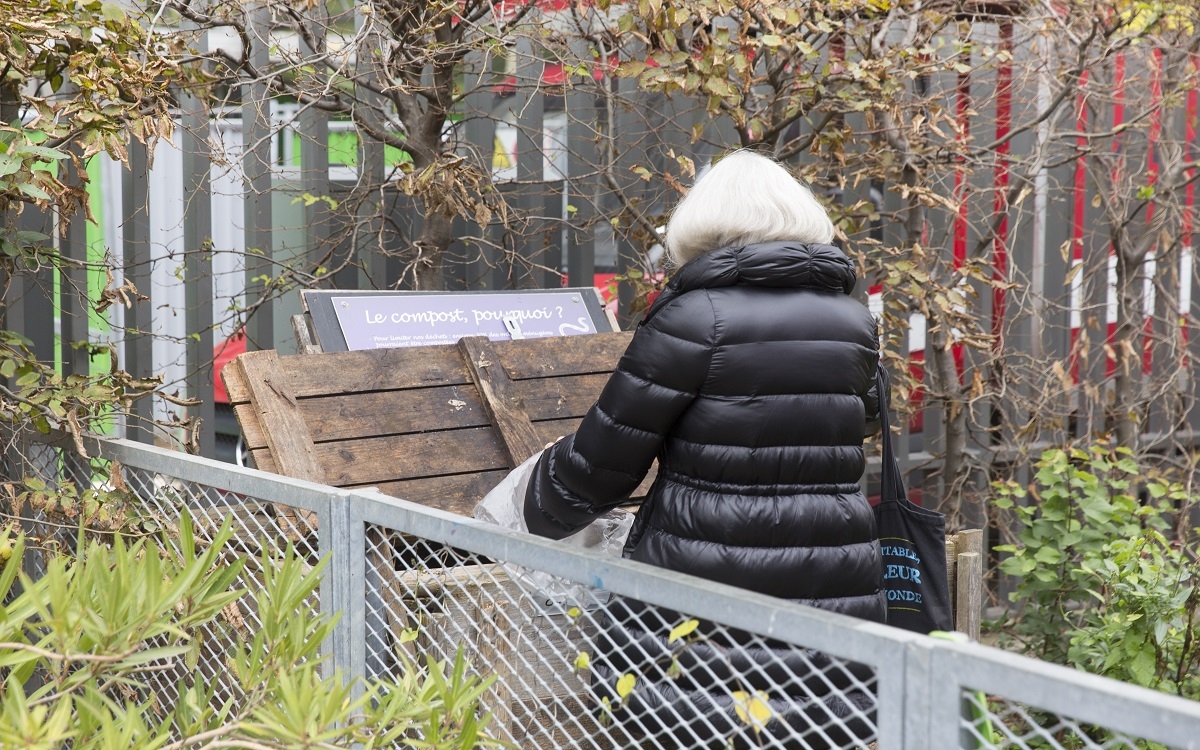 Une personne jette des déchets dans un compost situé dans un jardin partagé