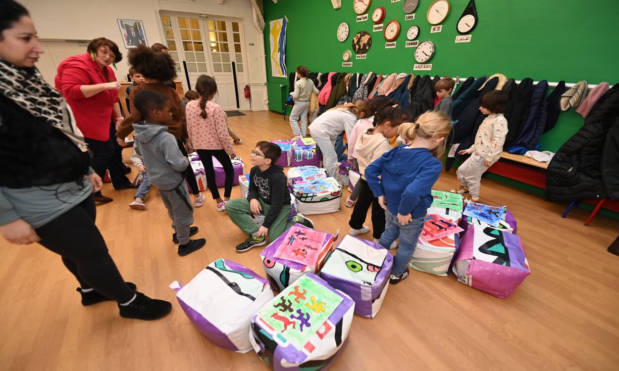 Un personne adulte, animatrice, s'adresse aux enfants qui regardent les dessins réalisés pendant la semaine d'immersion