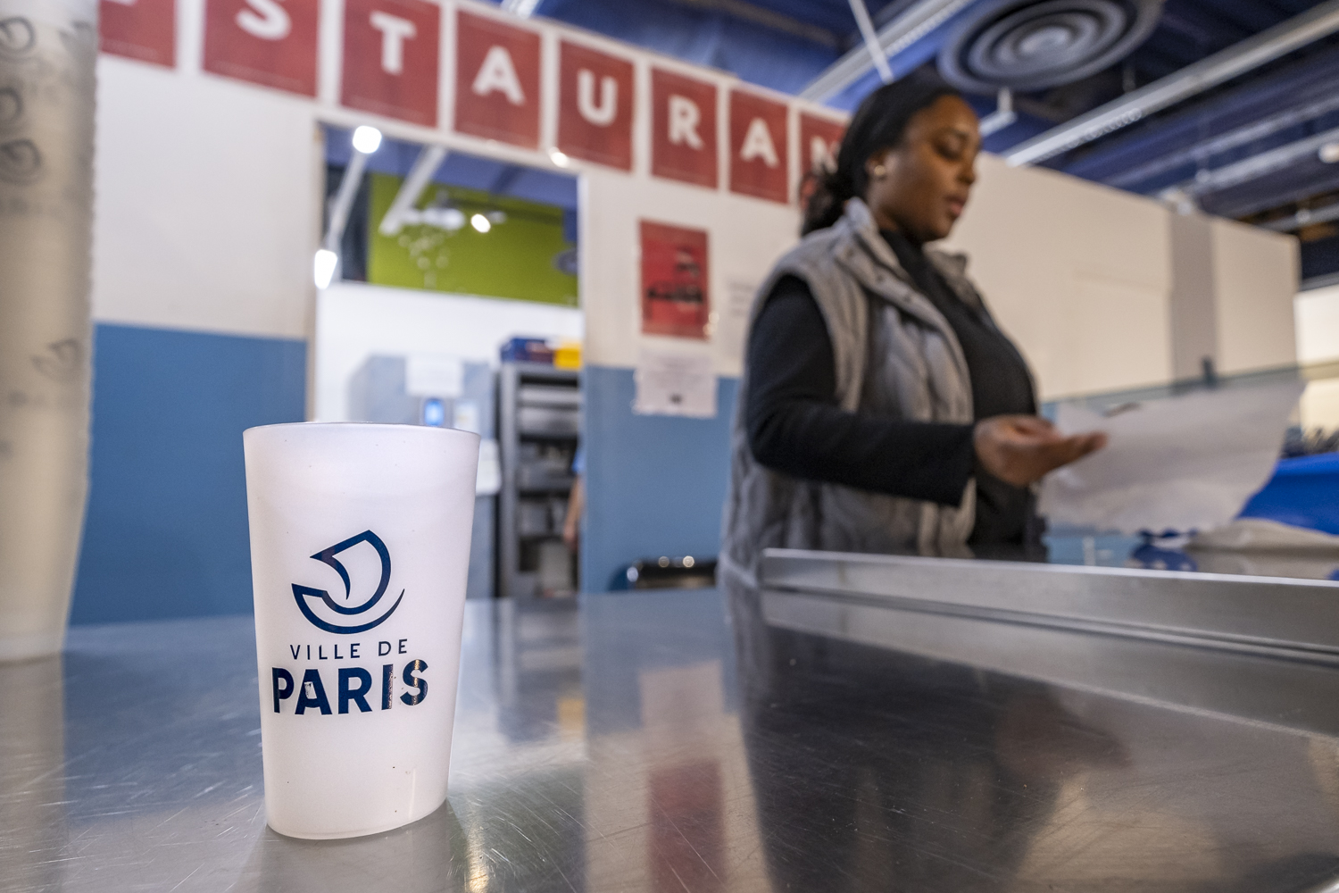 Une volontaire prépare des sets de couverts et des verres marqués "Ville de Paris" au centre d'accueil de la porte de Saint-Cloud