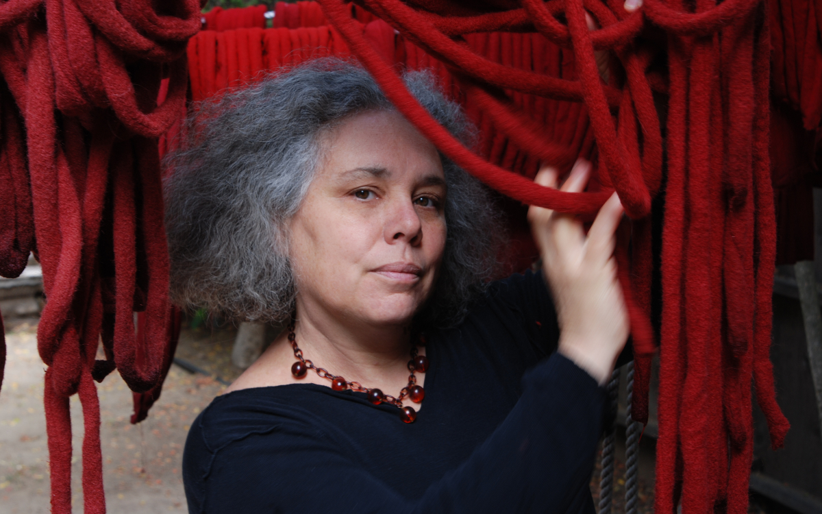 Portrait of American artist Alison Saar. She poses slightly in profile, with her left arm raised on red ropes.