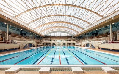 La piscine Georges Vallerey rénovée pour les Jeux dans le 20e, baignée de lumière avec sa charpente en bois spectaculaire.