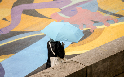 Le visuel représente une personne sous un parapluie, parcourant la fresque ASICS sur le quai de Seine. 