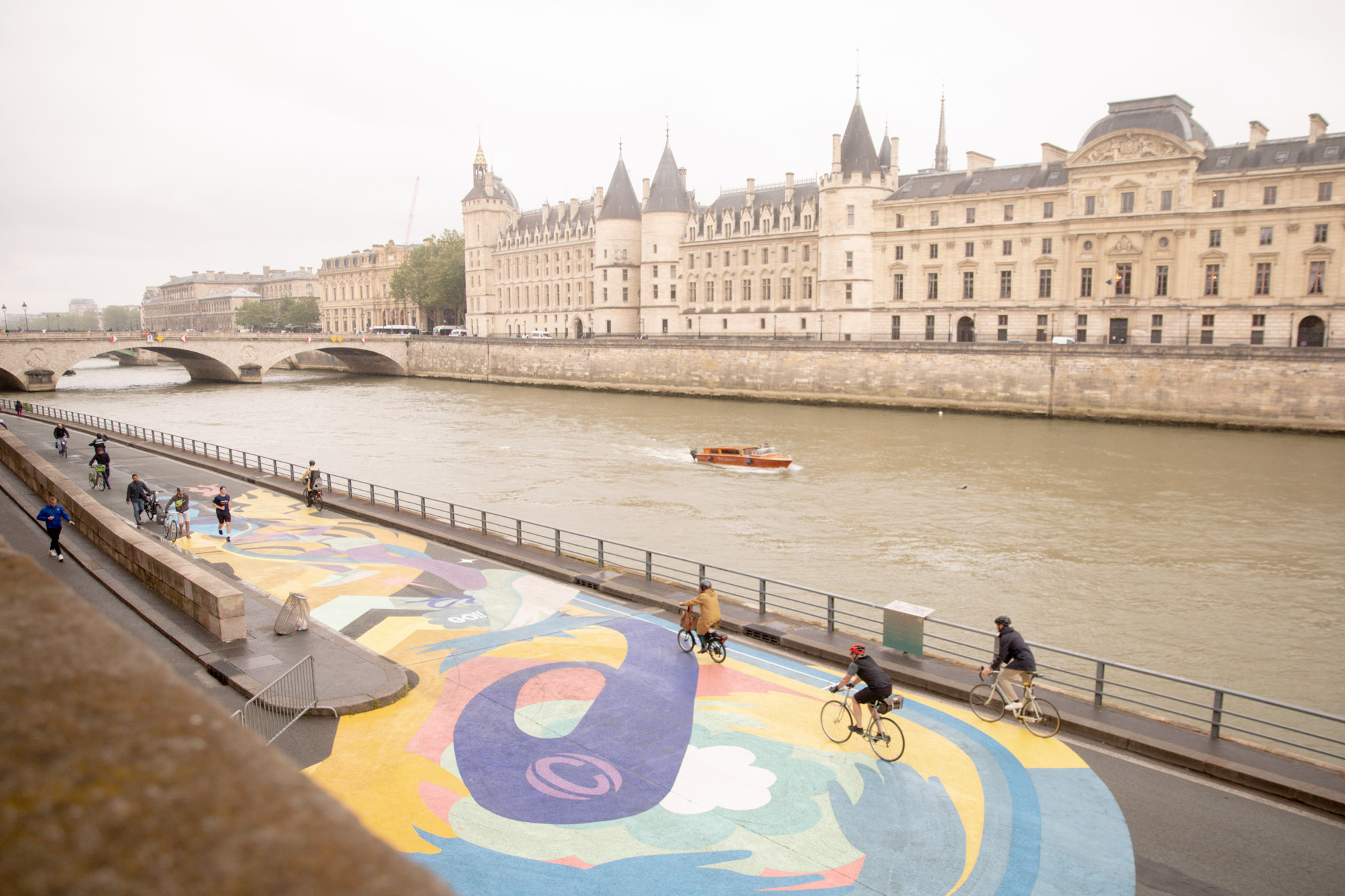 Des cyclistes passant sur la fresque ASICS sur le quai de Seine. 