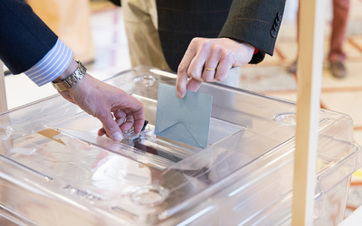 Une personne vote en déposant son enveloppe dans l'urne.