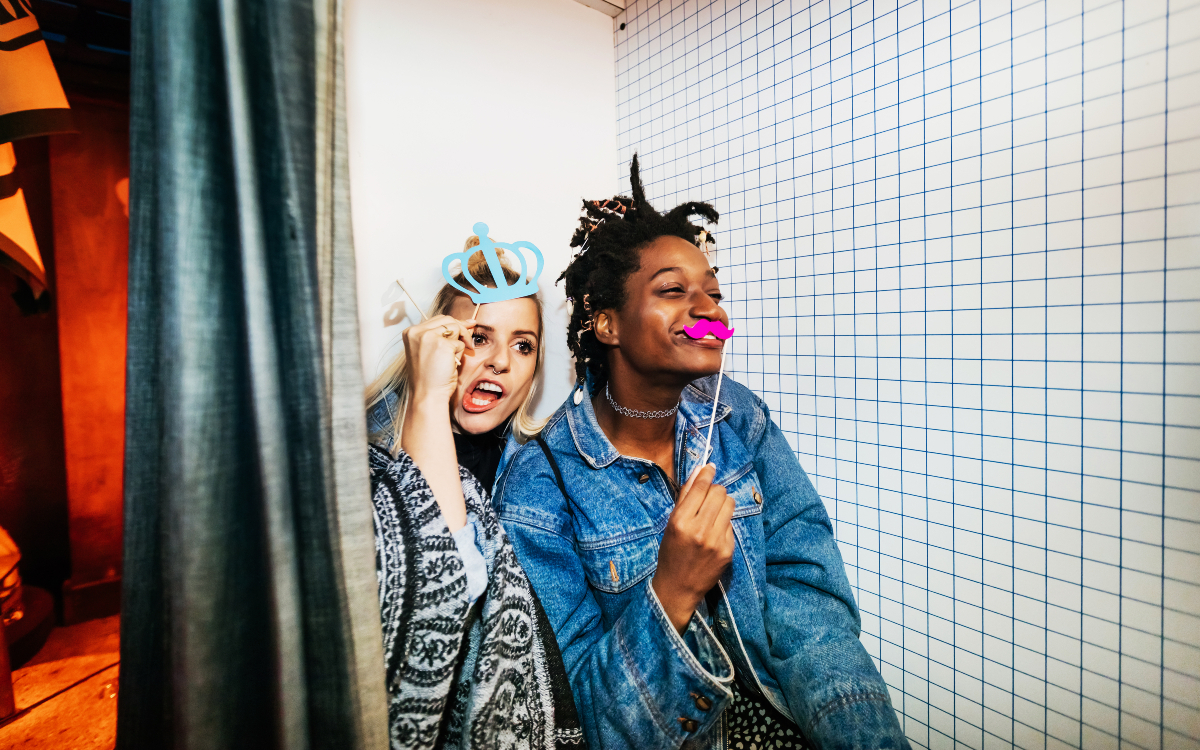 Deux amies s'amusent à se déguiser et à se prendre en photo dans un photobooth.