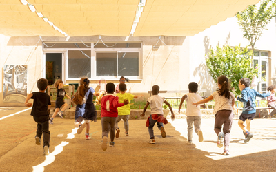 Des enfants courent sous le voile d'ombrage orange de la cour oasis de l'école Thionville, 19e