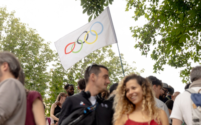 Deux personnes regardent la flamme passer sur le canal Saint-Martin, avec un drapeau olympique en arrière plan.