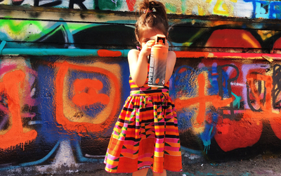 Une petite fille tient une bombe de peinture dans les mains devant un mur de street-art