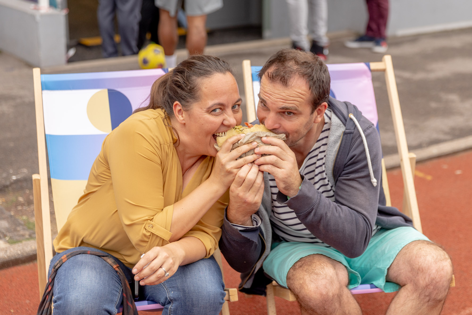 Deux spectateurs partagent un sandwich sur deux transats.