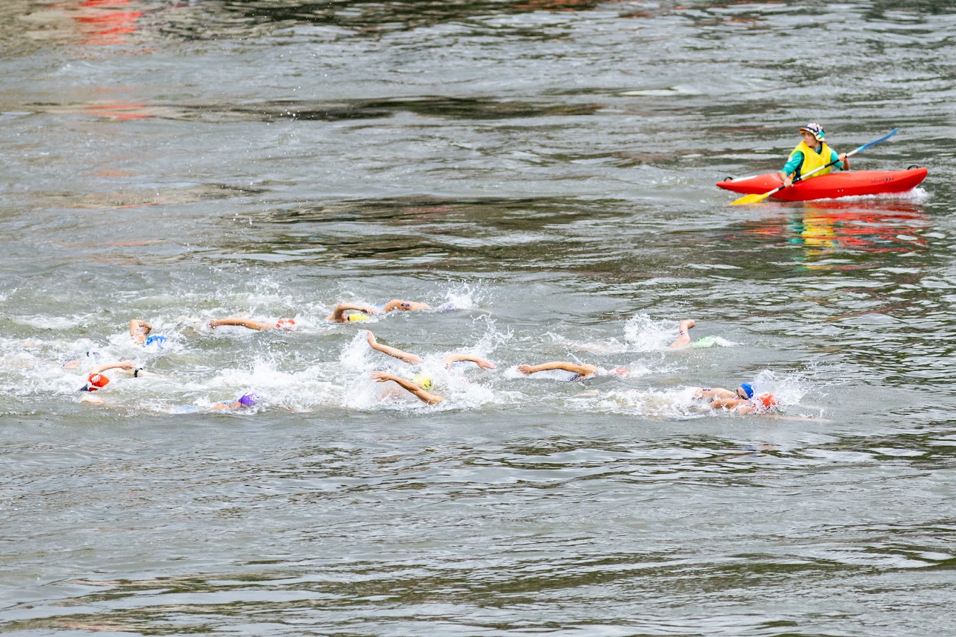 Des triathlètes dans la Seine avec un kayakiste qui observe les compétitrices.