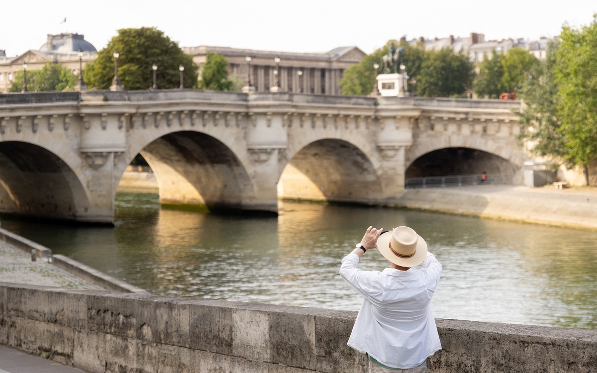Une personne portant un chapeau photographie le Pont Neuf