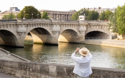 Une personne portant un chapeau photographie le Pont Neuf