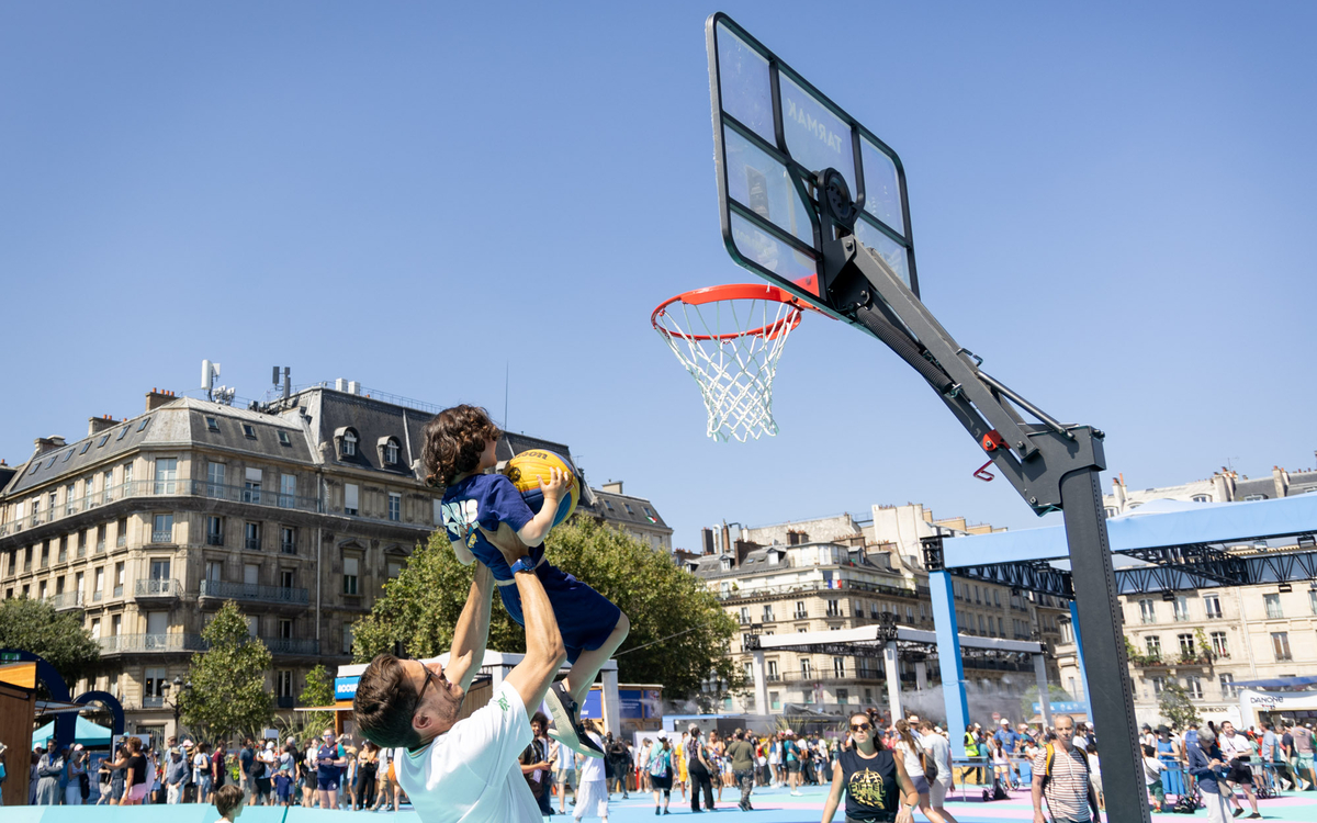 Un père aide son fils à marquer un but sur le terrain de basket de la terrasse des jeux. 