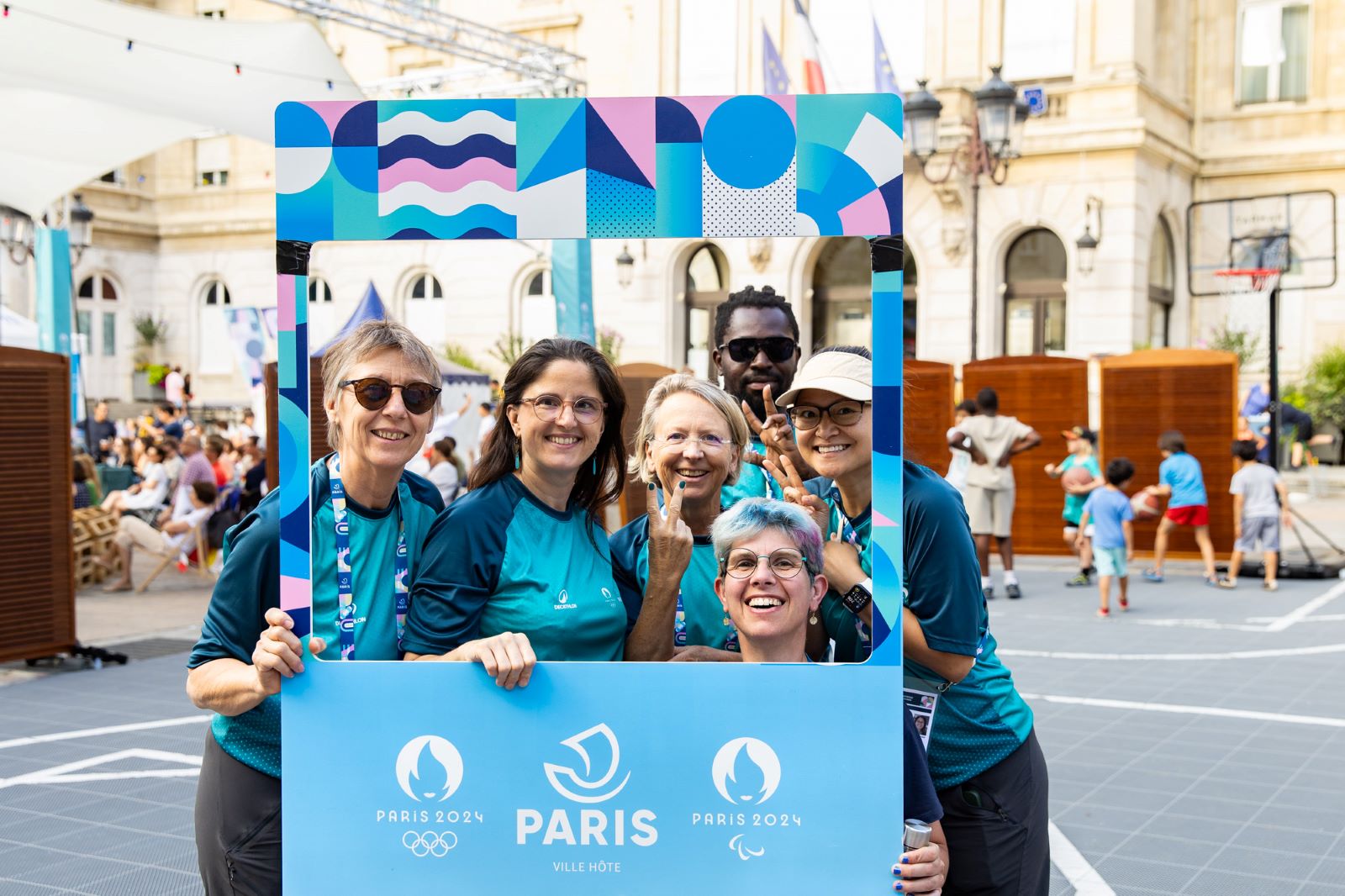 5 femmes et 1 hommes posent derrière un cadre géant aux couleurs des Jeux olympiques.