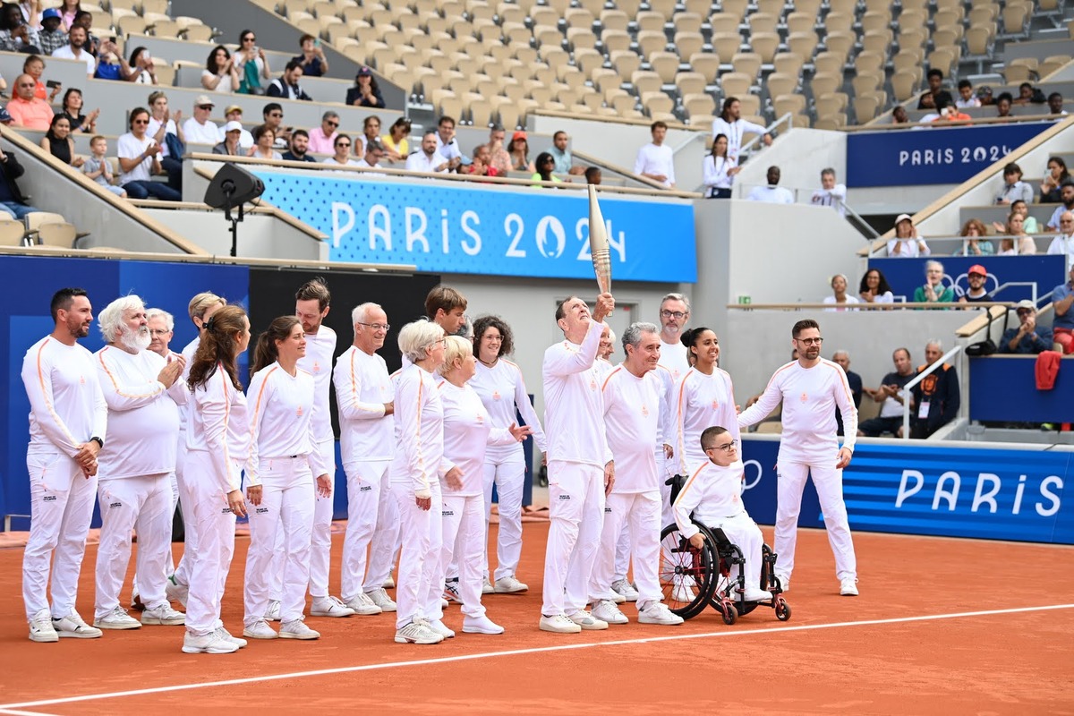 Un groupe de relayeurs hommes et femmes portent la flamme olympique sur le court Philippe Chatrier de Rolland Garros