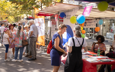 Photo du Forum des Associations 2023 organisé par la Mairie du 12e arrondissement de Paris. Plusieurs personnes se promènent et échangent sous des barnums installés sur une place. Les stands des associations locales sont alignés, offrant des informations et des activités aux visiteurs dans une ambiance conviviale et animée.