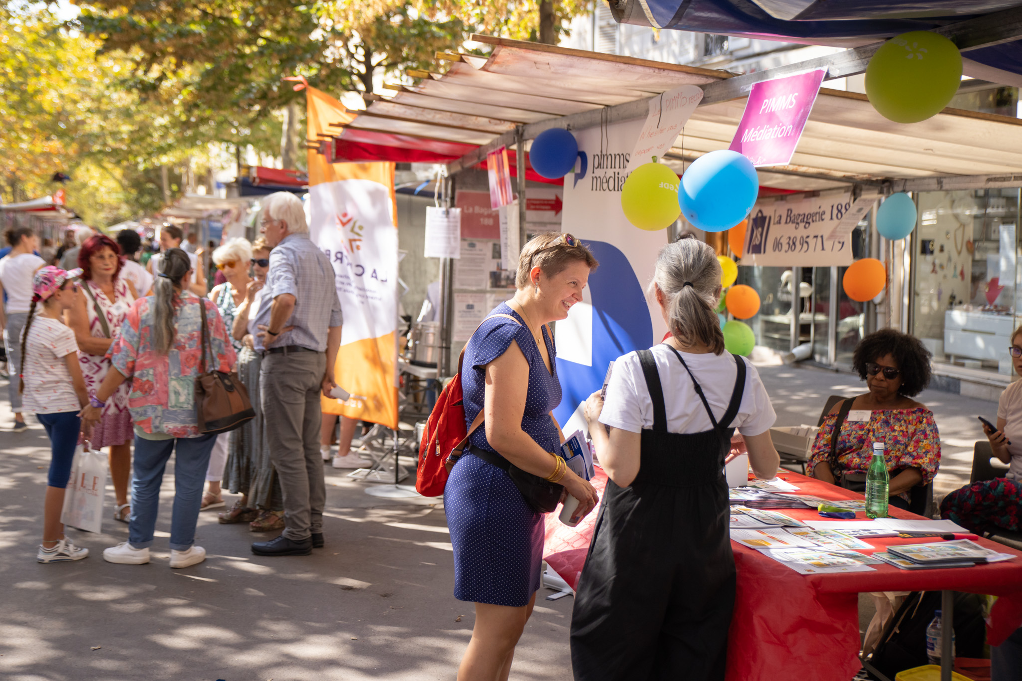 Photo du Forum des Associations 2023 organisé par la Mairie du 12e arrondissement de Paris. Plusieurs personnes se promènent et échangent sous des barnums installés sur une place. Les stands des associations locales sont alignés, offrant des informations et des activités aux visiteurs dans une ambiance conviviale et animée.