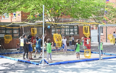 Des enfants jouent au home ball dans un cage en filets dans la cour de l'ecole Rouannet