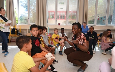 Une animatrice de l'académie des langues accroupie s'adresse aux enfants d'un centre de loisirs assis autour d'elle