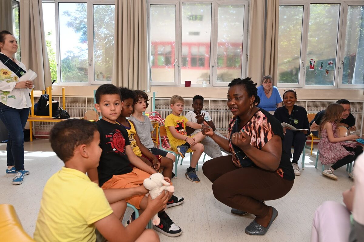 Une animatrice de l'académie des langues accroupie s'adresse aux enfants d'un centre de loisirs assis autour d'elle