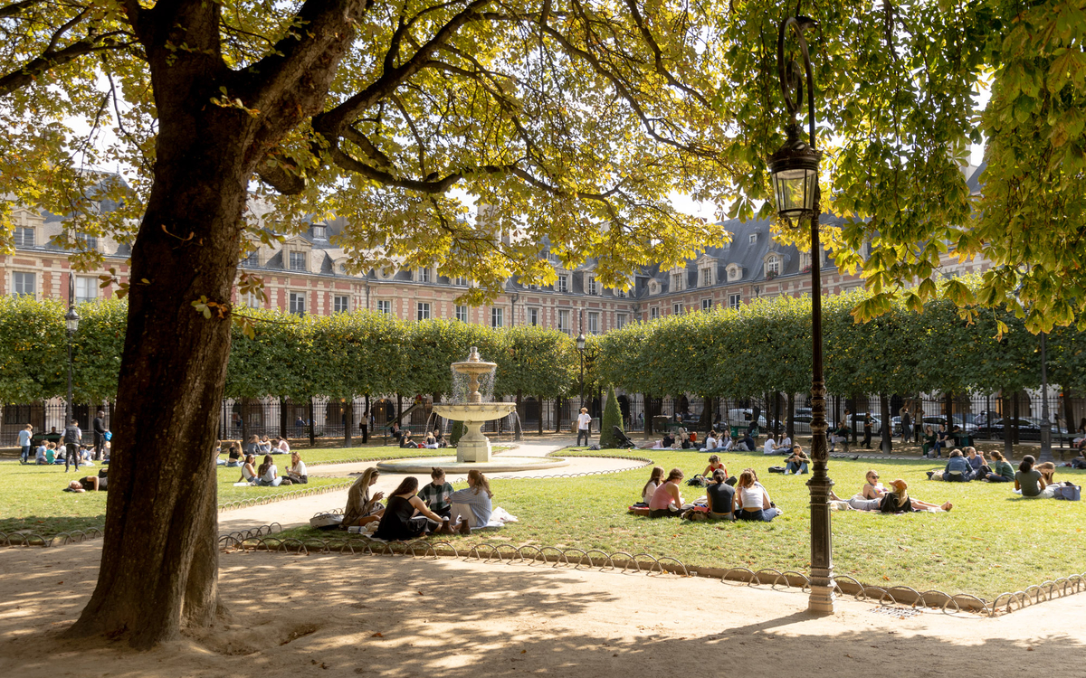 Des personnes profitant du soleil sur les pelouses de la place des Vosges. 