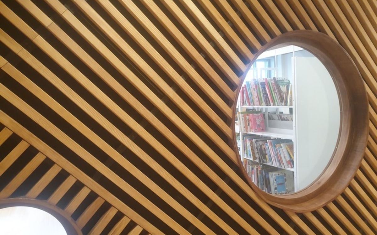 Vue sur des étagères de livre au travers d'un hublot de la bibliothèque des Batignolles.