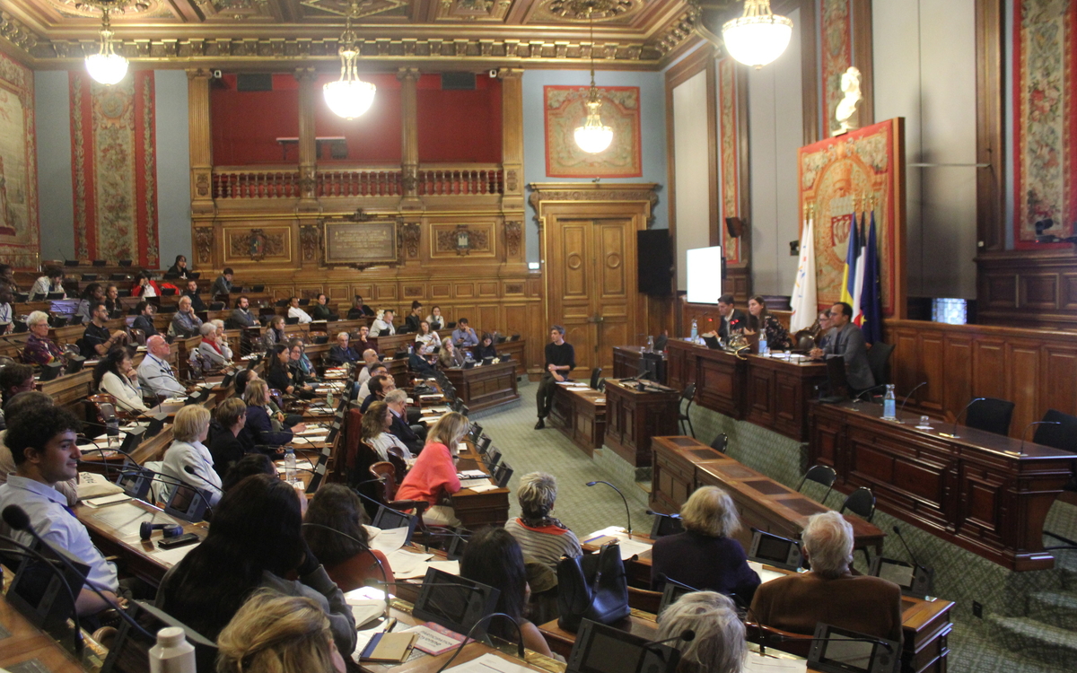 Un groupe de personne est installé dans la salle du Conseil de Paris en face de la tribune, occupée par des élus de Paris