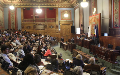 Un groupe de personne est installé dans la salle du Conseil de Paris en face de la tribune, occupée par des élus de Paris