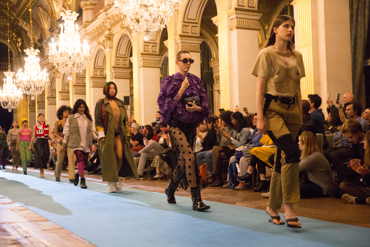 Maroussia Rebecq investit la salle des fêtes de l’Hôtel de Ville d’un défilé de mode de monsieur et de madame tout le monde. Une célébration des possibilités infinies du stylisme, à partir de vêtements du quotidien, de la pop culture.