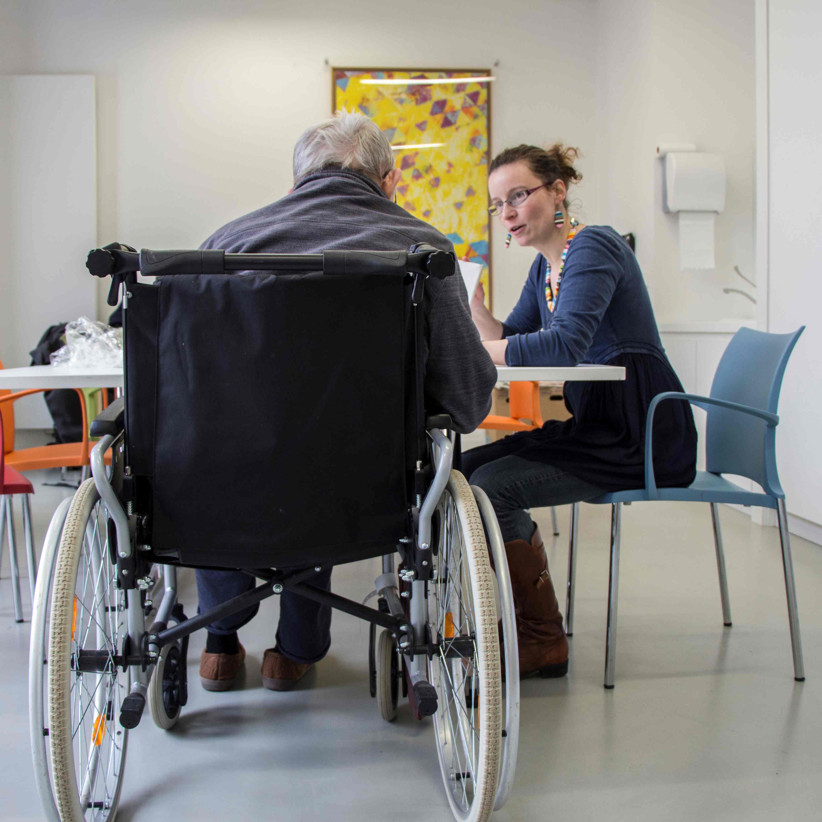 une femme présente un tableau à une personne en fauteuil roulant