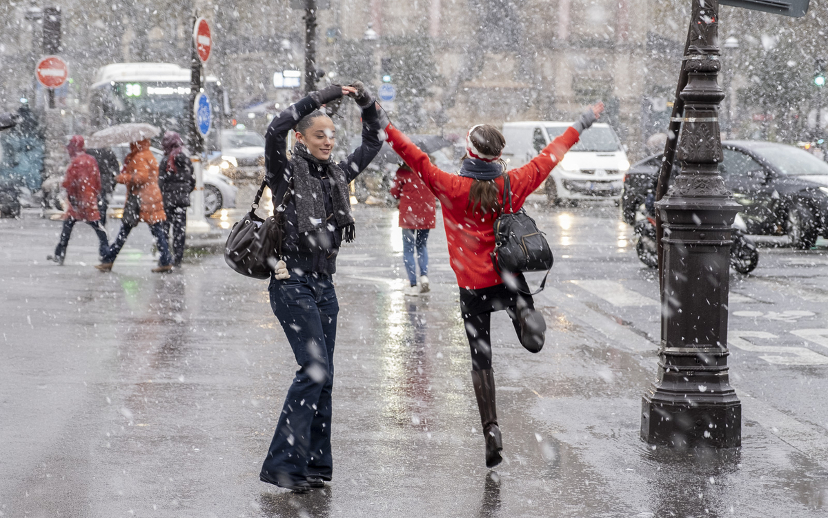Des passantes dansent de joie sous la neige.