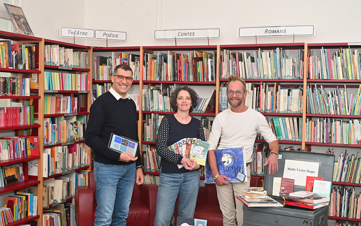 Trois animateurs du Centre Paris Lecture posent devant une bibliothèque avec des ouvrages, une tablette numérique et un carnet de dessin dans leurs mains