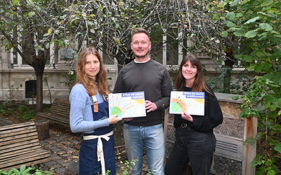 Trois animateurs de l'Académie du climat posent dans la cour de la mairie du 4e arrondissement avec des affiches sur la terre et le soleil dans leurs mains