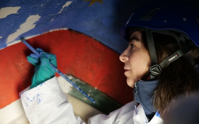 Pinceau à la main, une femme restaure une peinture bleue