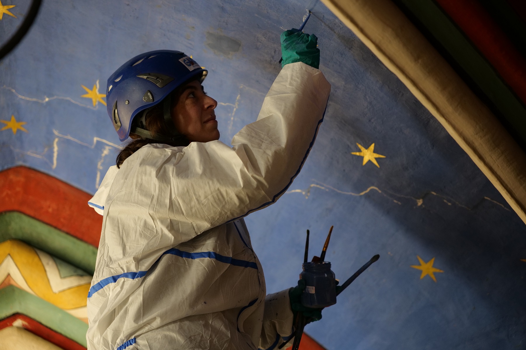 Une femme avec un casque et un pinceau à la main, en train de restauré un ciel étoilé